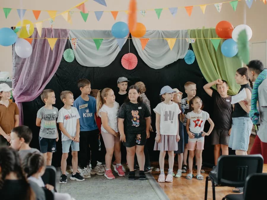 Children singing together on stage at the village camp